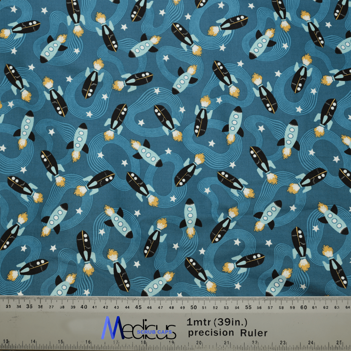 This Medicus Scrub Caps fabric features black and white rockets with orange flames, blue windows on a starry blue background, ideal for crafting a Space Ships Scrub Cap. Includes a 1-meter (39 inches) ruler at the bottom. Perfect for healthcare professionals.