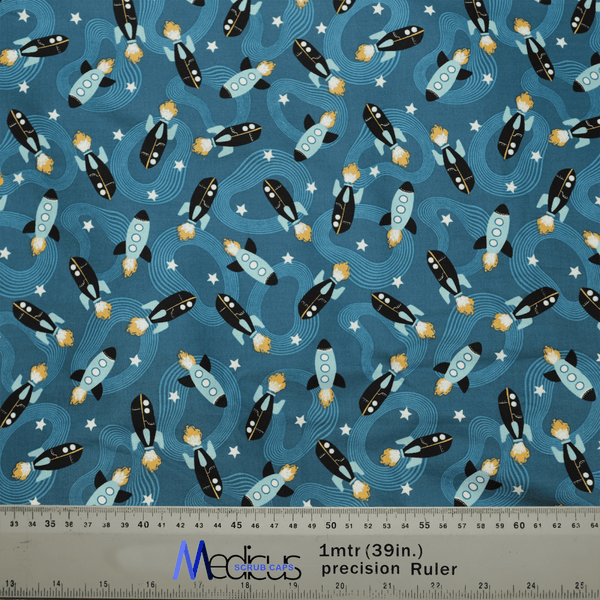 This Medicus Scrub Caps fabric features black and white rockets with orange flames, blue windows on a starry blue background, ideal for crafting a Space Ships Scrub Cap. Includes a 1-meter (39 inches) ruler at the bottom. Perfect for healthcare professionals.