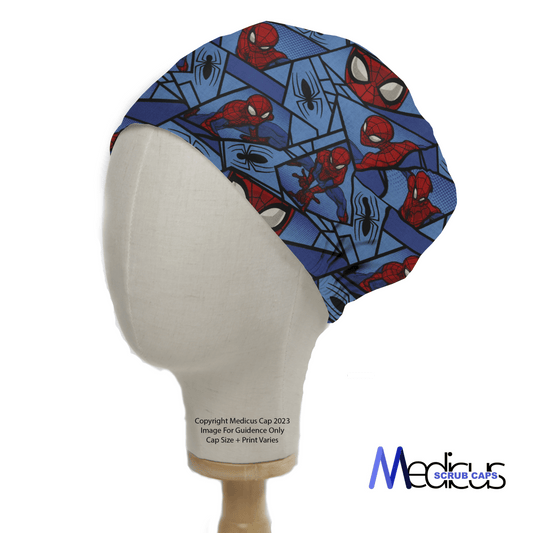 A mannequin head displays a Spiderman Comic Web Grid Scrub Cap in blue, with red and black spider-themed illustrations and superhero poses. The reusable cap is by Medicus Scrub Caps, its logo visible beside the head.