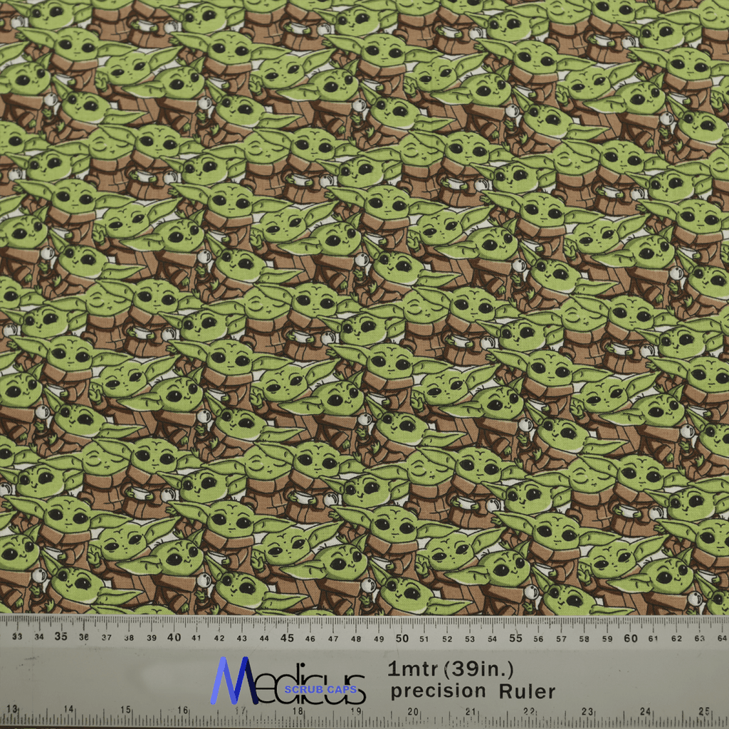 Patterned fabric with a small green alien in a brown robe and white scarf adds intergalactic charm. A 1-meter precision ruler shown for scale. Ideal for making a Star Wars Baby Yoda Crowd Scrub Cap by Medicus Scrub Caps with style.