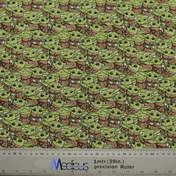 Patterned fabric with a small green alien in a brown robe and white scarf adds intergalactic charm. A 1-meter precision ruler shown for scale. Ideal for making a Star Wars Baby Yoda Crowd Scrub Cap by Medicus Scrub Caps with style.
