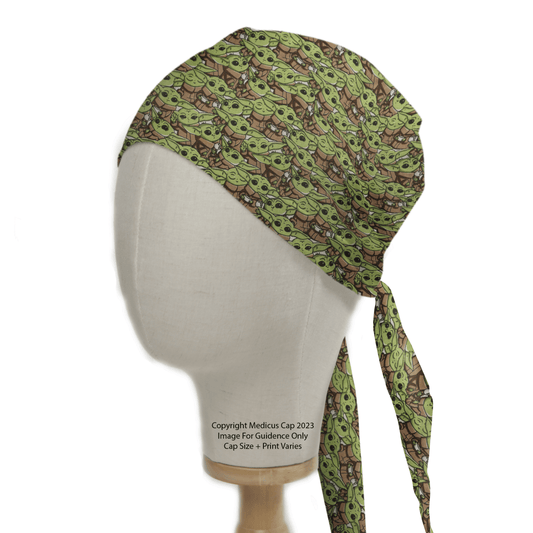 A mannequin head showcases the Star Wars Baby Yoda Crowd Scrub Cap by Medicus Scrub Caps, featuring a green cartoon character pattern on a brown background. It ties at the back with two tails hanging down, offering an intergalactic charm with sustainable style.