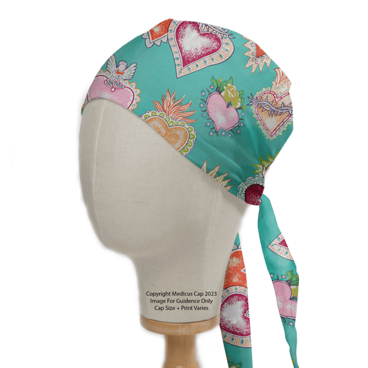 A mannequin displays the Tattoo #1 Love Hearts Scrub Cap by Medicus Scrub Caps, featuring a teal cap with colorful tattoo-inspired hearts and floral patterns. The sustainable cap offers comfort and a tied back design. Image text: Copyright Medicos Cap 2023 and Image For Guidance Only Cap Size & Print Varies.