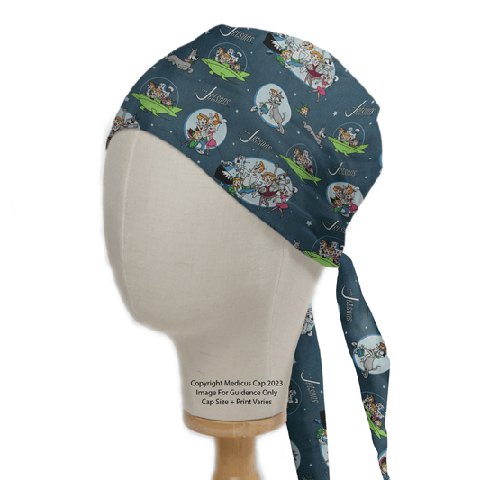 A mannequin head displays The Jetsons Family Scrub Cap by Medicus Scrub Caps, combining retro-futuristic style with a playful space theme. It features characters and spaceships on dark blue fabric, with a reusable tie-back design and copyright details included.