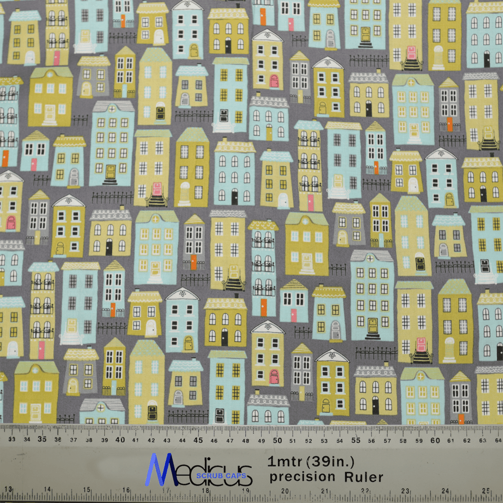 The Townhouse Scrub Cap by Medicus Scrub Caps is adorned with pastel-colored house illustrations on a gray background. Featuring a ruler for measurements in meters and inches, this charming cap is perfect for healthcare professionals seeking sustainable, reusable options.