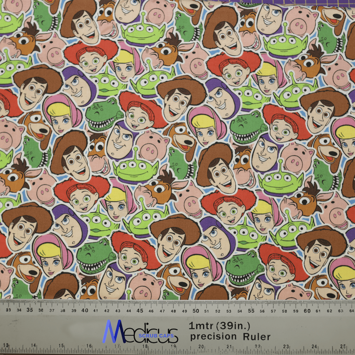 The Medicus Scrub Caps Toy Story Faces Cutout fabric, ideal for scrub caps, features cowboys, space rangers, dinosaurs, and pigs. A ruler at the bottom offers measurements in inches and centimeters—perfect for healthcare professionals wanting a playful touch.