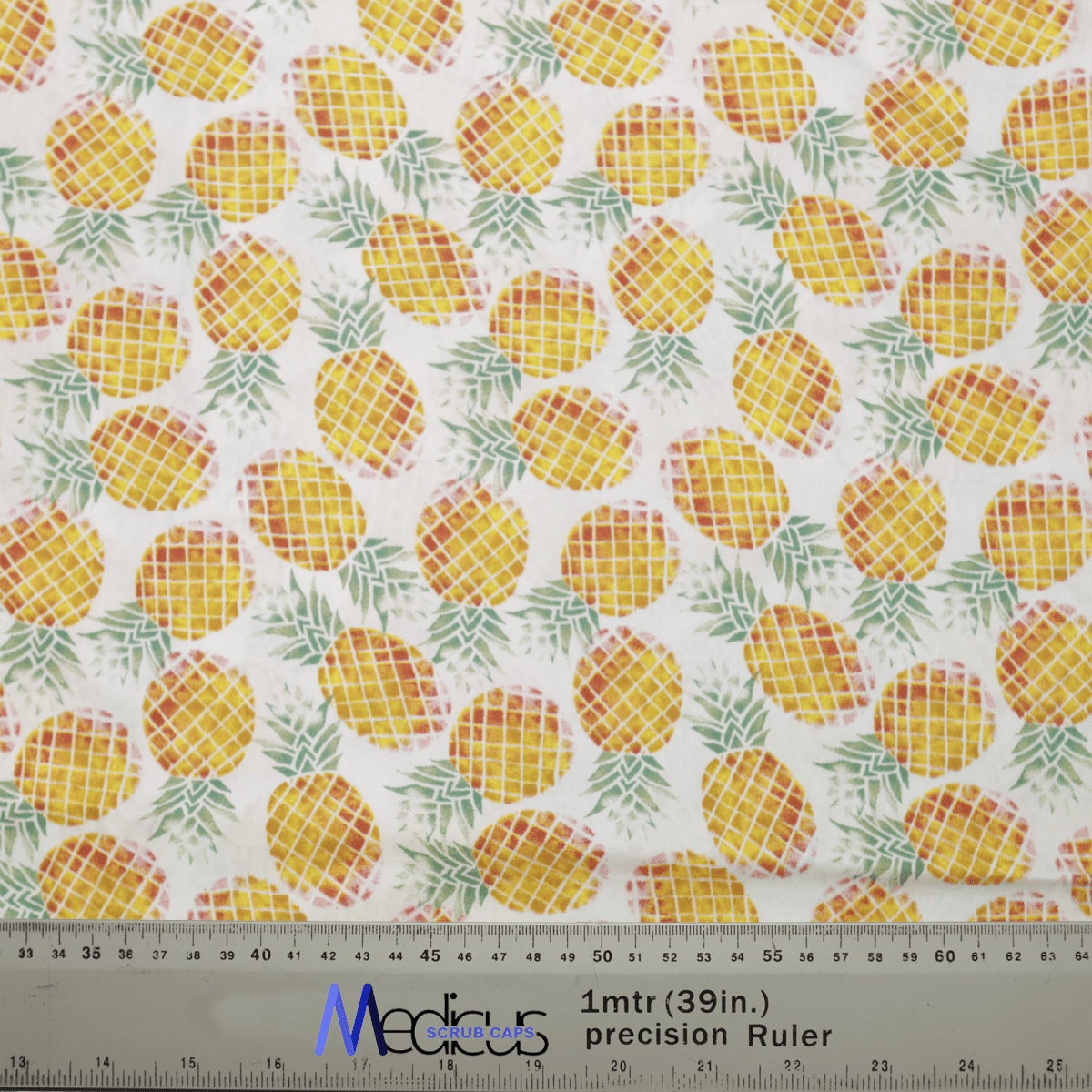 The Medicus Scrub Caps Tropical Pineapples Scrub Cap features a vibrant yellow pineapples and green leaves pattern on white, with a ruler at the bottom for inch and centimeter measurements, showcasing its eco-friendly design as part of a reusable healthcare collection.