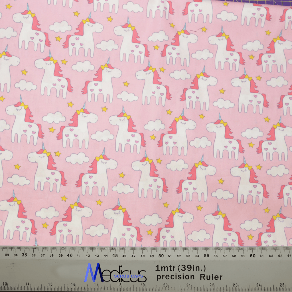 The Unicorn Cartoon Pink Scrub Cap by Medicus Scrub Caps showcases white unicorns with rainbow manes and tails, yellow-starred collars, on a pink background with white clouds and yellow stars. A ruler in centimeters and inches is included, making it ideal for crafting sustainable scrub caps.