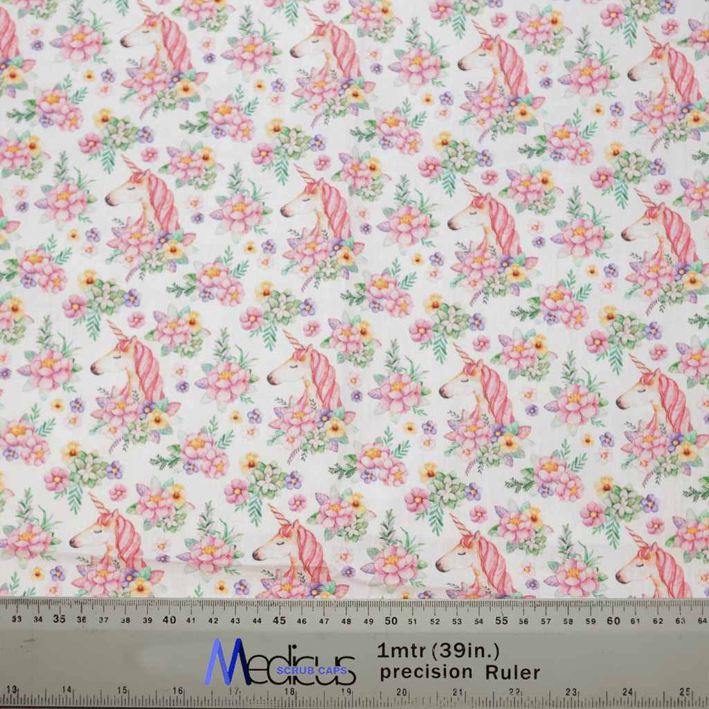 The Medicus Scrub Caps Unicorns Flower Power Scrub Cap features fabric with pink unicorns and colorful flowers on a white background, ideal for crafting. A transparent ruler marks centimeters and inches for precise cutting.