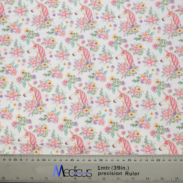 The Medicus Scrub Caps Unicorns Flower Power Scrub Cap features fabric with pink unicorns and colorful flowers on a white background, ideal for crafting. A transparent ruler marks centimeters and inches for precise cutting.