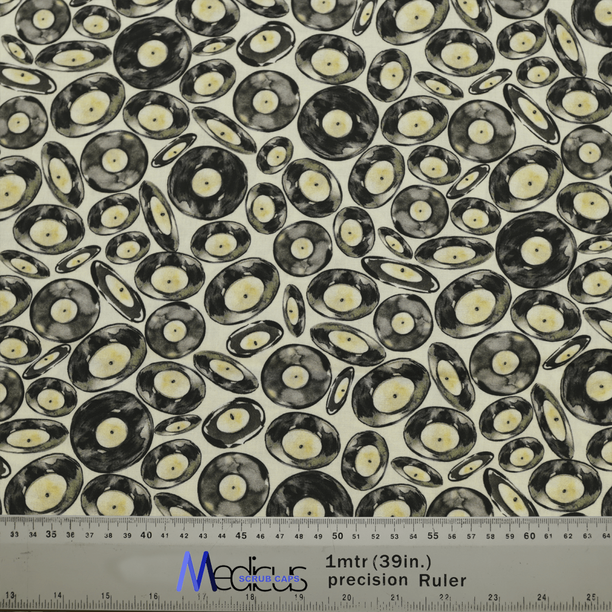 The Medicus Scrub Caps Vinyl Discs Scrub Cap fabric displays black vinyl records on a light background, perfect for music lovers. A ruler with inches and centimeters at the bottom aids crafting in sustainable healthcare settings.
