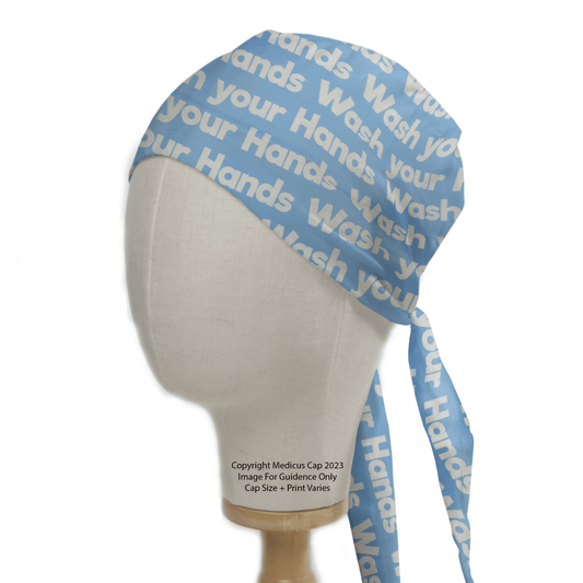 Medicus Scrub Caps Wash Your Hands light blue scrub cap, featuring repeated white text, is displayed on a wooden base. Ideal for healthcare professionals, it ties at the back and promotes sustainable healthcare practices.