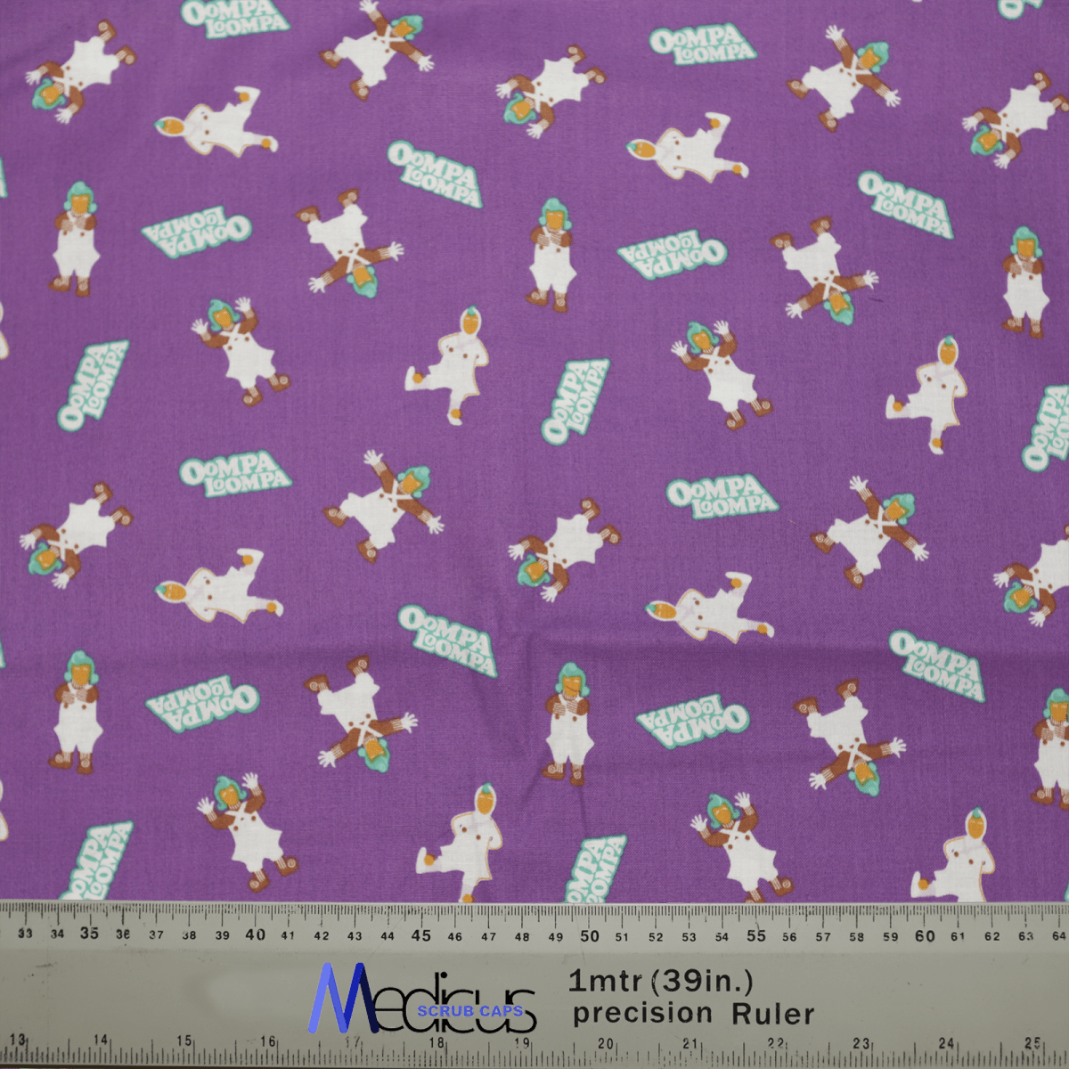 The Medicus Scrub Caps Willy Wonka Oompa Loompa features colorful Willy Wonka character illustrations and Ompa Loompa text on purple fabric. A ruler at the bottom highlights its whimsical design, ideal for crafting scrub caps.