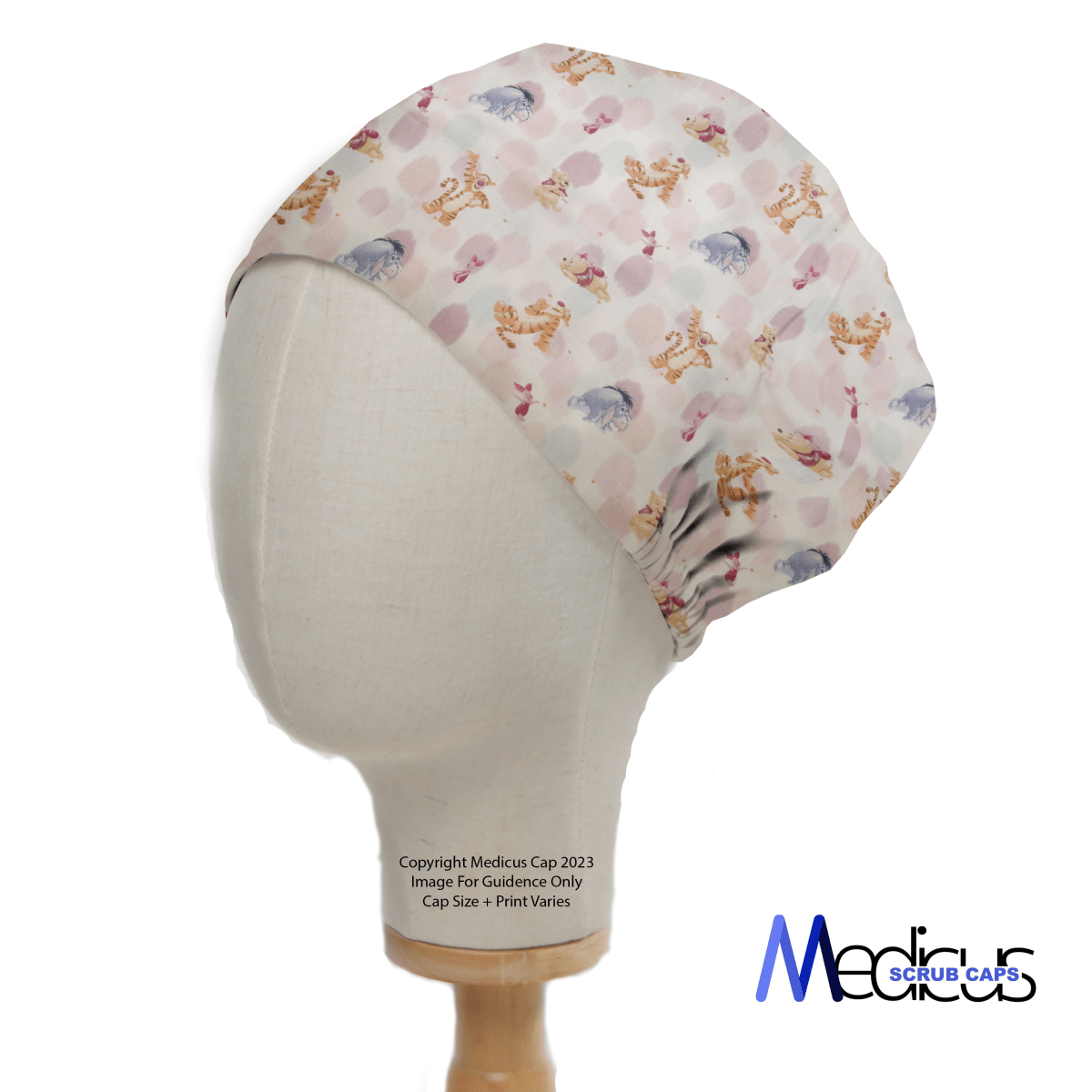 A mannequin head dons the Medicus Scrub Caps Winnie The Pooh + Friends Finger Paint scrub cap, showcasing assorted animal patterns on a light background, with a logo in the bottom right corner.