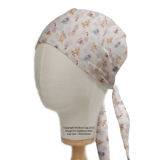 A mannequin head displays the Medicus Scrub Caps Winnie The Pooh + Friends Finger Paint Scrub Cap, featuring a tie-back design and eco-friendly materials with playful animal images on a white background.