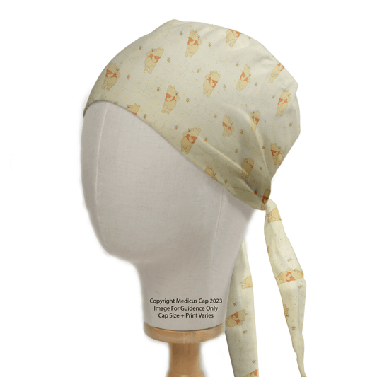 A mannequin head displays the Winnie The Pooh Honey + Bees Scrub Cap by Medicus Scrub Caps, featuring a charming animal print with cartoon-like dogs in playful poses. This light-colored cap ties at the back with long straps, adding a whimsical touch to any medical ensemble.