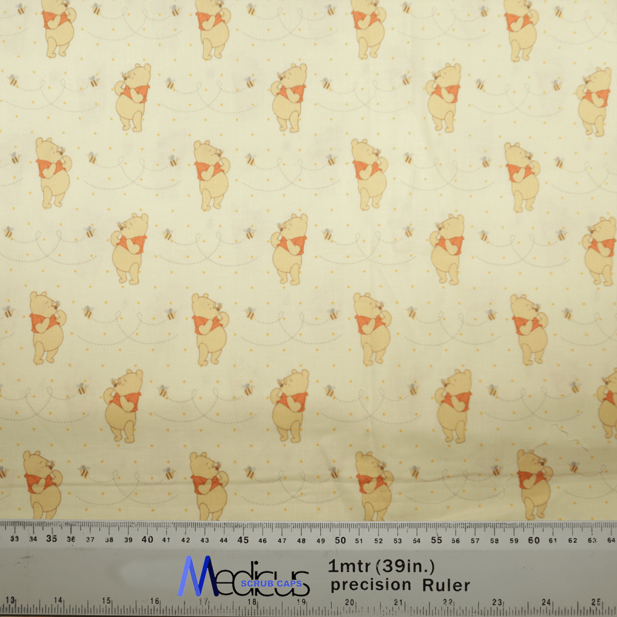 The Winnie The Pooh Honey + Bees Scrub Cap by Medicus Scrub Caps showcases a playful pattern of Winnie The Pooh and bees. It features a ruler with measurements in centimeters and inches, perfect for creating whimsical scrub cap designs.