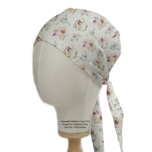 Side view of a Winnie The Pooh + Piglet scrub cap by Medicus Scrub Caps on a mannequin head. The cap features charming illustrations with a long tie at the back, ideal for customizing with embroidery or choosing eco-friendly healthcare options.