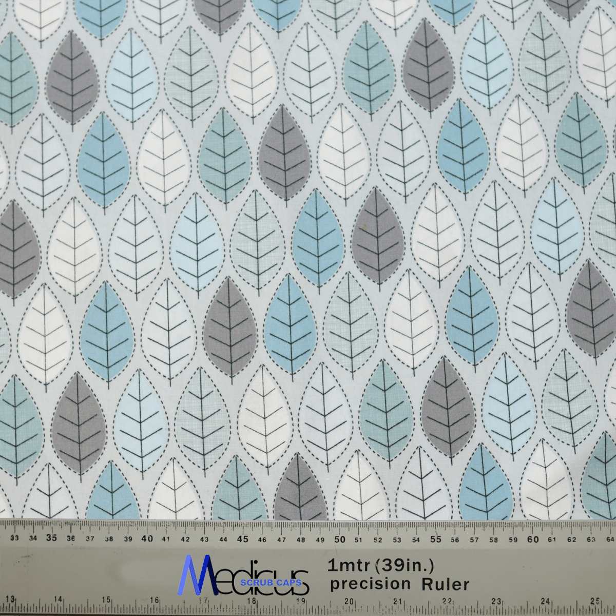 Medicus Scrub Caps Winter Leaves Scrub Cap features a calming leaf pattern in blue, gray, and white. The leaves are arranged in alternating rows, and a metal ruler at the bottom provides measurements in both meters and inches.
