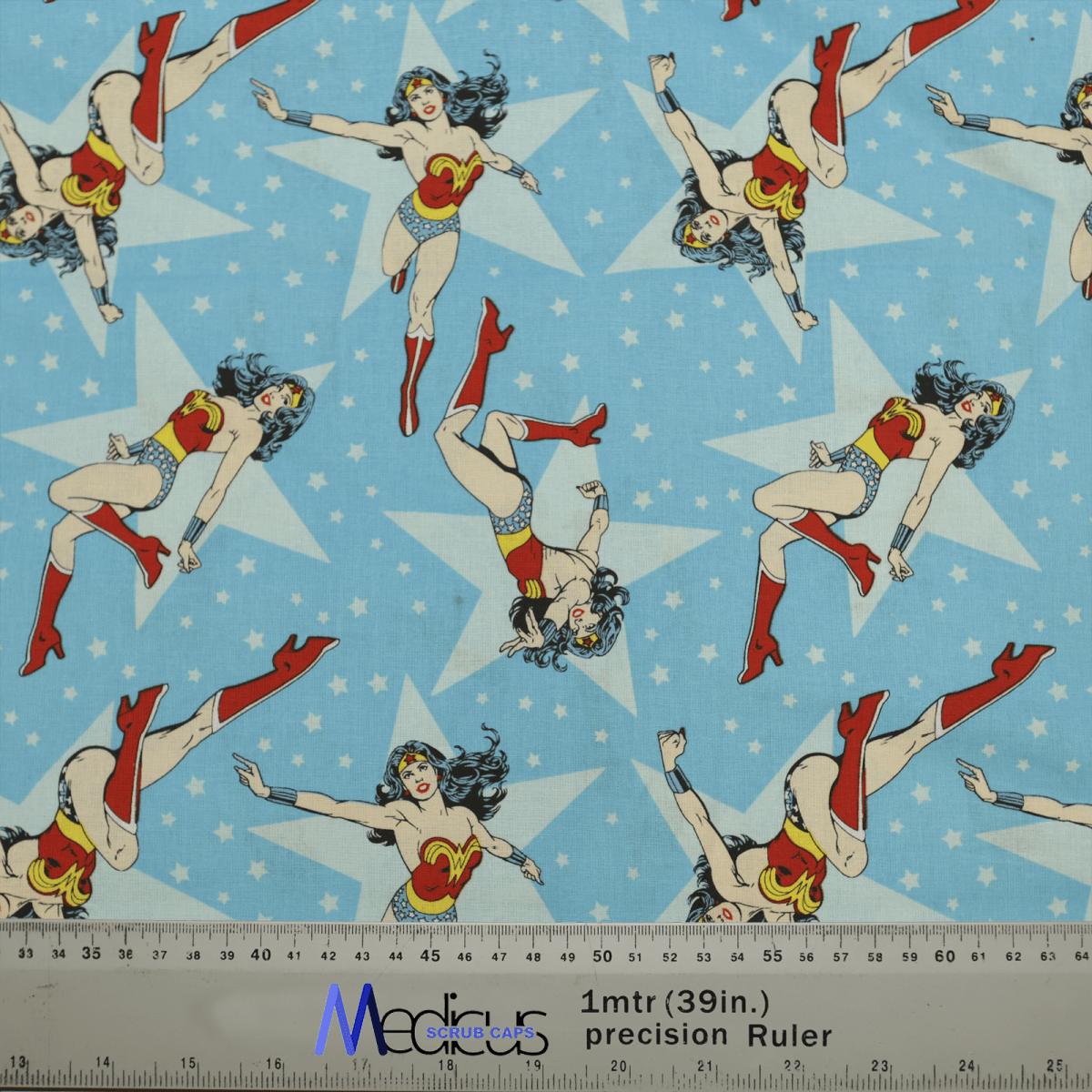 Comic-style superheroine images with stars on a blue background grace the Wonder Woman Blue Scrub Cap from Medicus Scrub Caps, inspiring healthcare professionals. A ruler at the bottom displays measurements in centimeters and inches, ideal for eco-conscious healthcare settings.