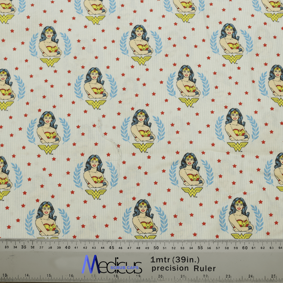 The Wonder Woman Crest Scrub Cap by Medicus Scrub Caps features a comic-style superhero woman with the Wonder Woman crest, red stars, and measurements in inches and centimeters along the bottom—ideal for healthcare professionals seeking style.