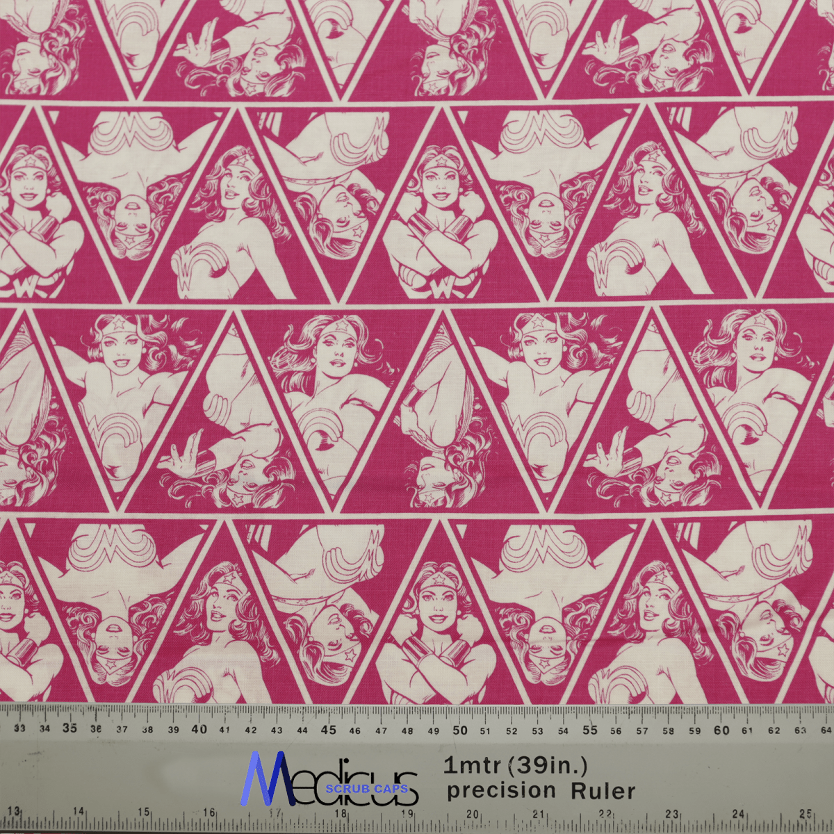 The Wonder Woman Pink Diamonds Scrub Cap by Medicus Scrub Caps features pink and white geometric fabric with superhero women in various poses within triangles. An empowering essence flows through the design, with a Medidas Gráficas ruler at the bottom measuring in inches and centimeters.