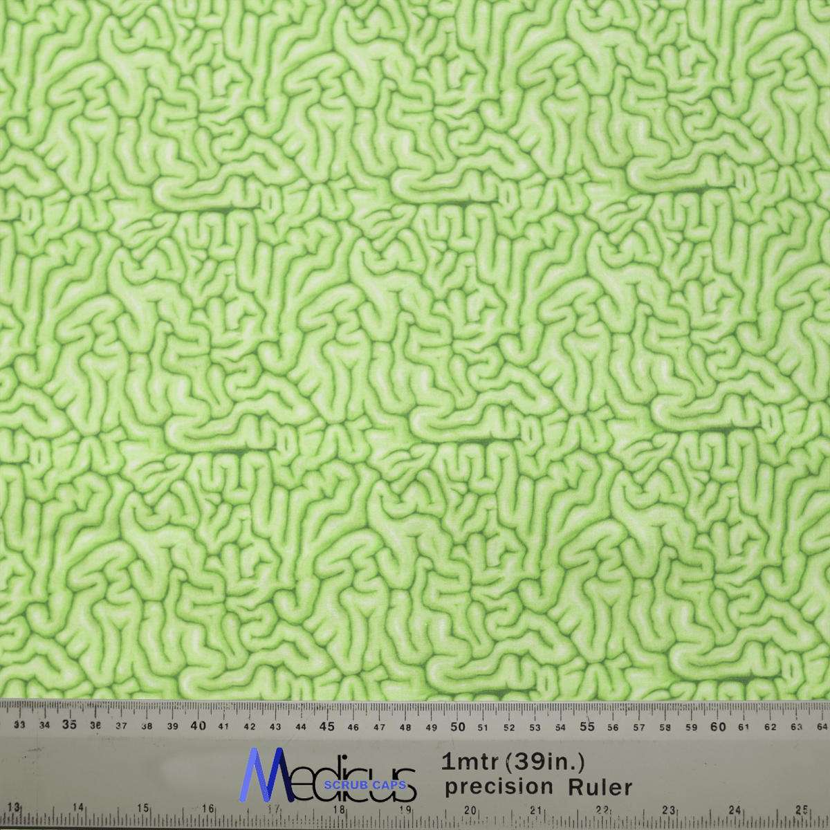 A close-up of Medicus Scrub Caps Zombie Brain Green Scrub Cap fabric, featuring an abstract squiggly pattern. A ruler below displays centimeters and inches alongside Medicus, appealing to healthcare professionals interested in eco-friendly options.